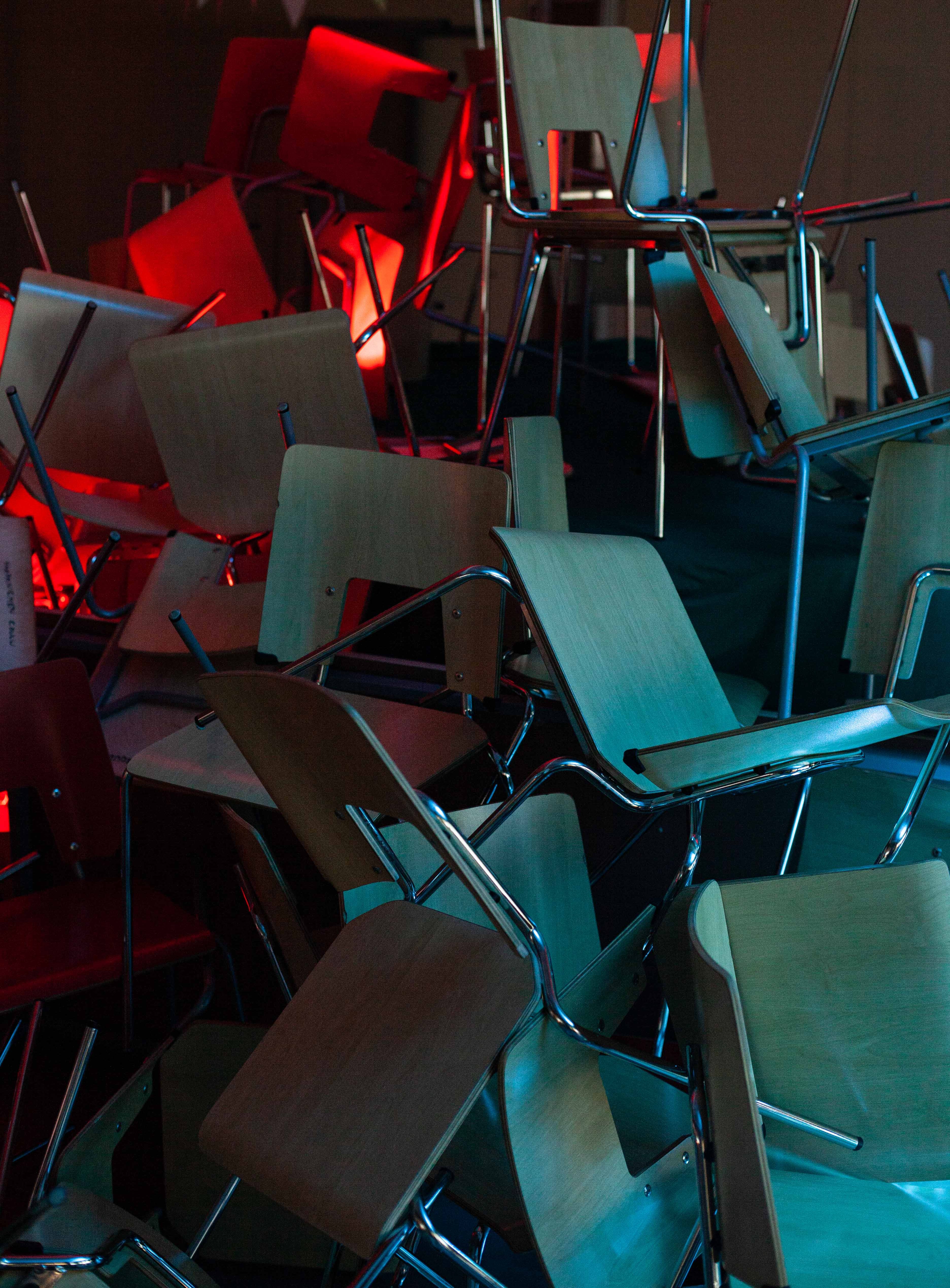 A pile of chairs in low theatrical light of red and blue colors.
